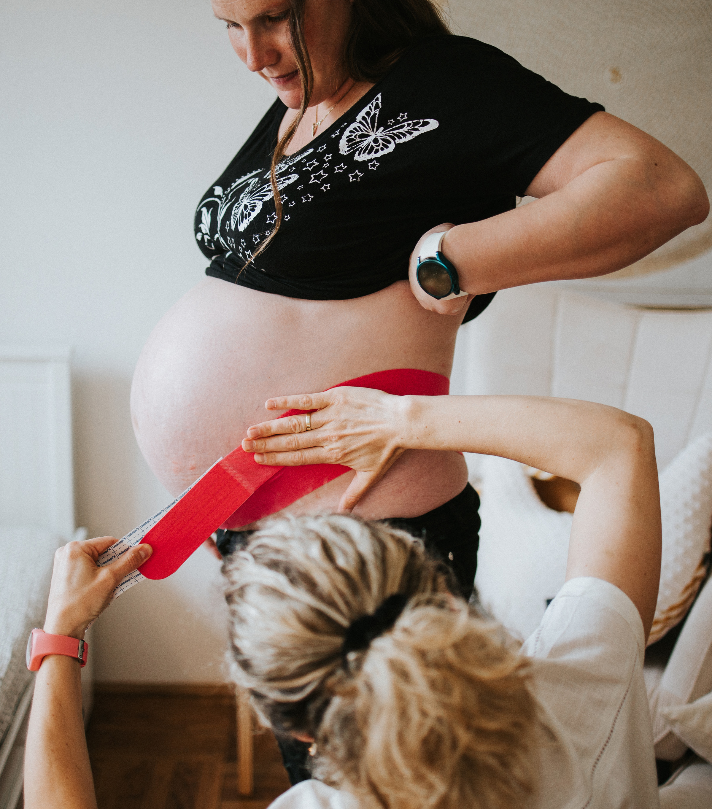 Hebamme klebt Kinesio-Tape auf den Bauch einer Schwangeren